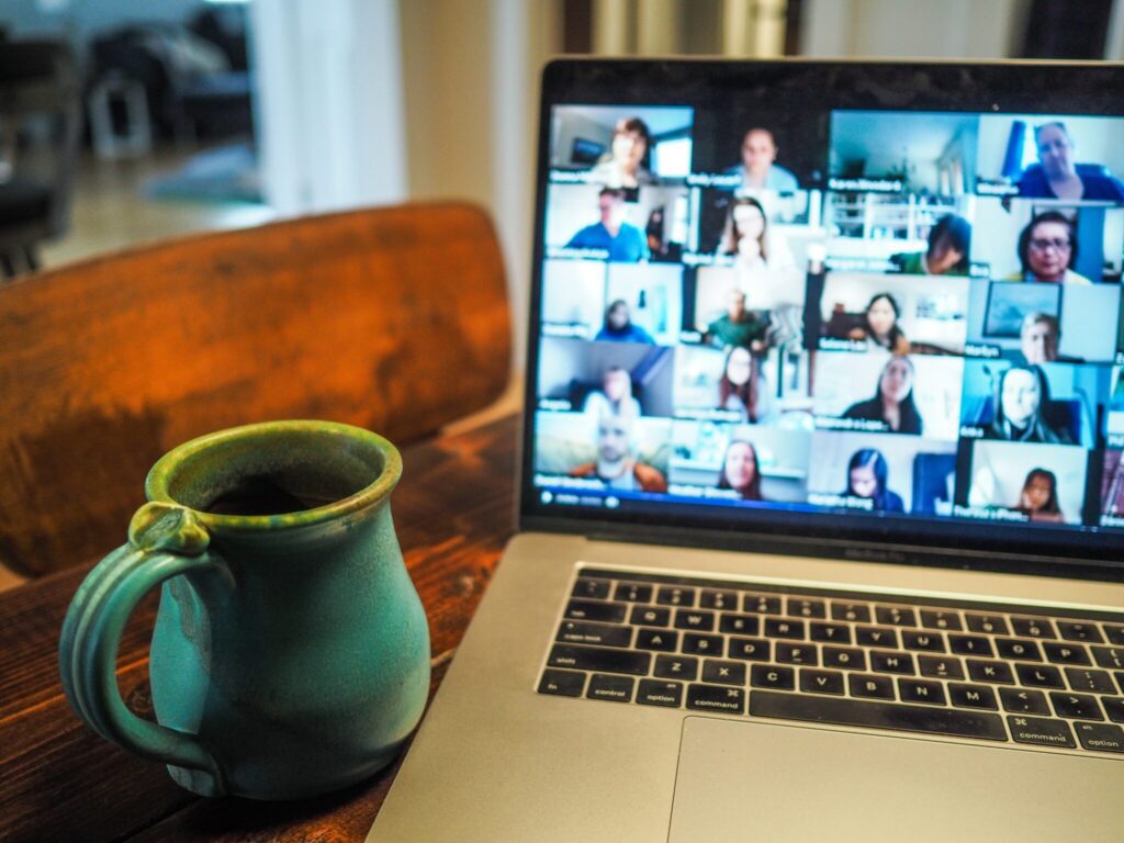 A laptop on a table, open to a video call with may participants. There's a cup next to it.