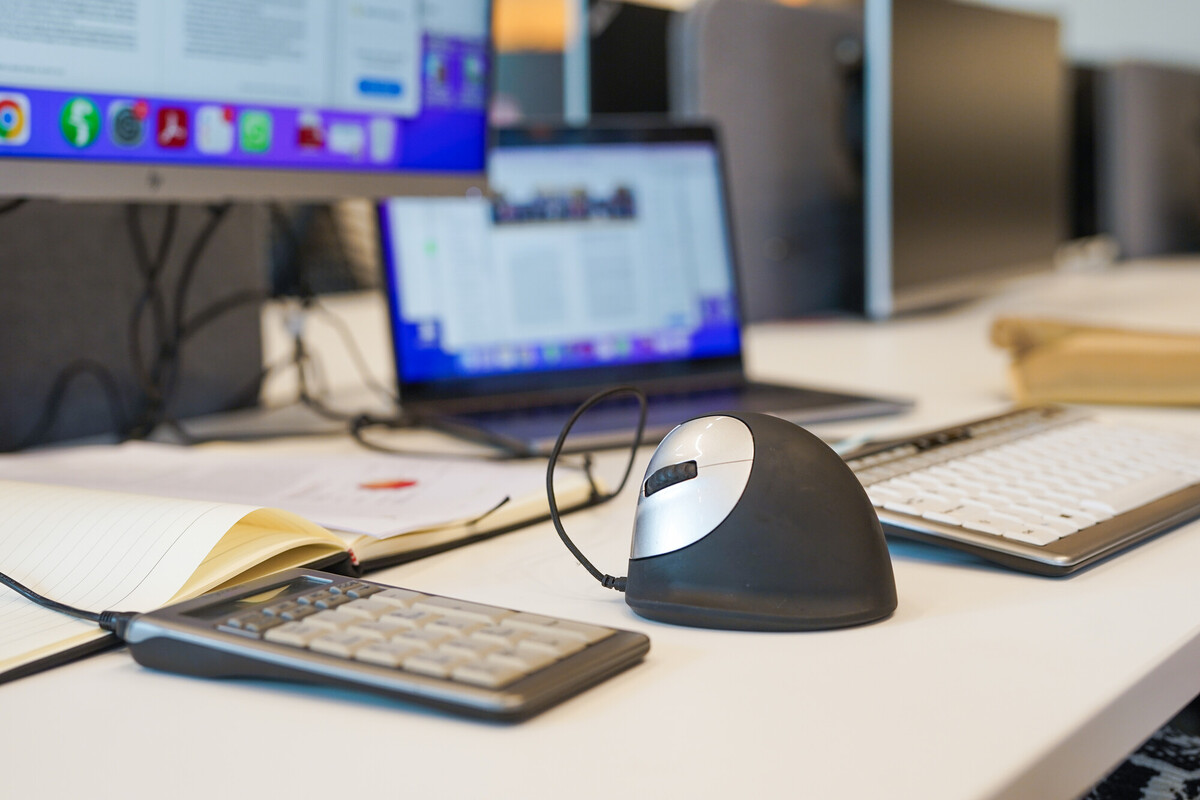 An ergonomic mouse, calculator, laptop and other equipment on a desk.