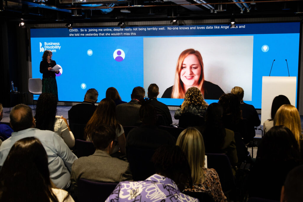 Diane Lightfoot on stage at the Business Disability Forum 2024 Annual Conference, with Angela Matthews video-conferencing on a screen.