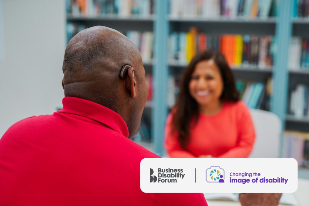 A man who is Deaf and wears a hearing aid chats to a colleague.