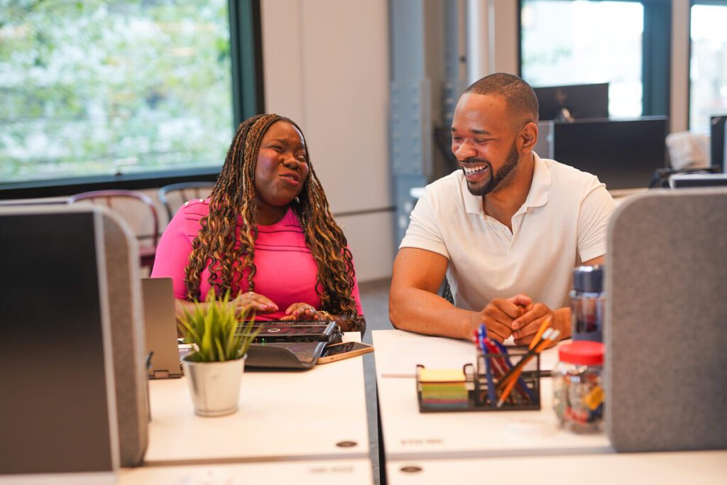 Blind professional laughs with a colleague as they work on a braille notetaker.