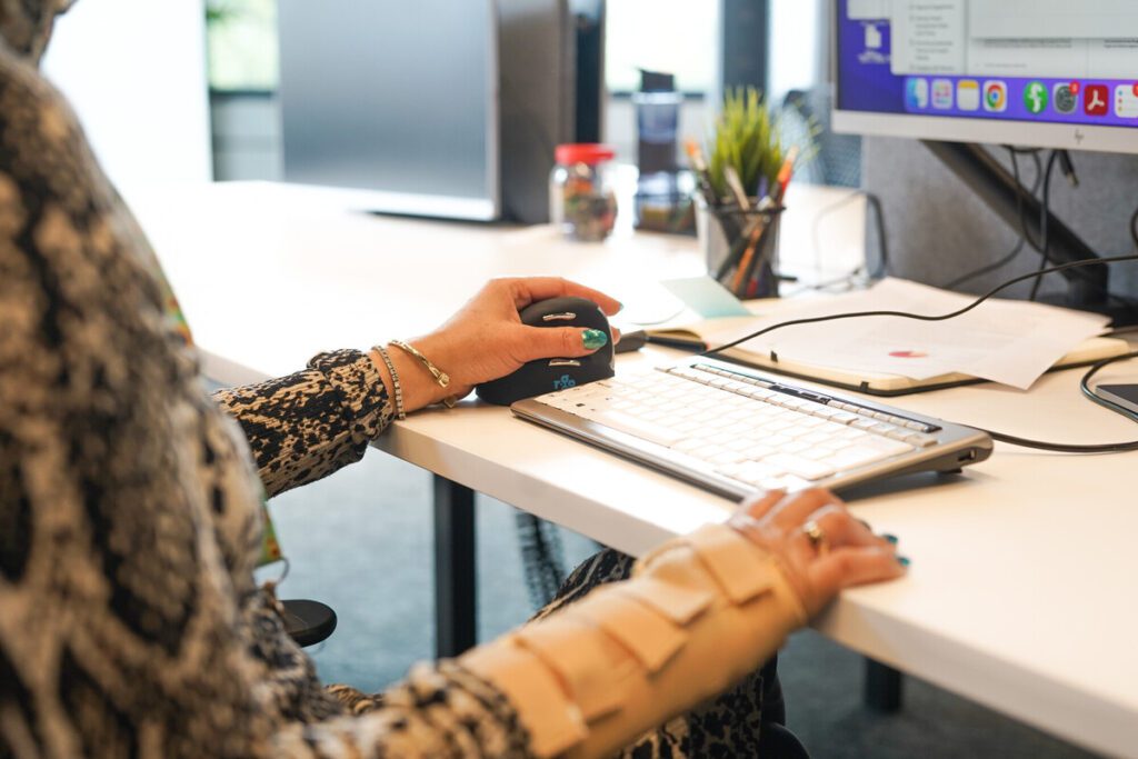 Close up on a professional's hands as they work at a desk using an ergonomic mouse. They are wearing a wrist support.