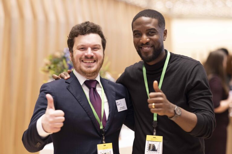 2 delegates posing with thumbs up at an event.