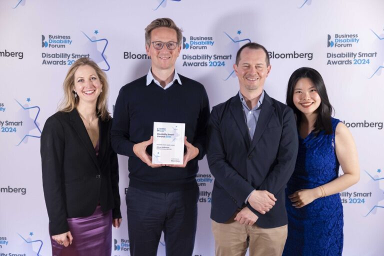 5 people posing at an event. One is holding a trophy. Behind them is a backdrop with the Disability Smart Award logo.