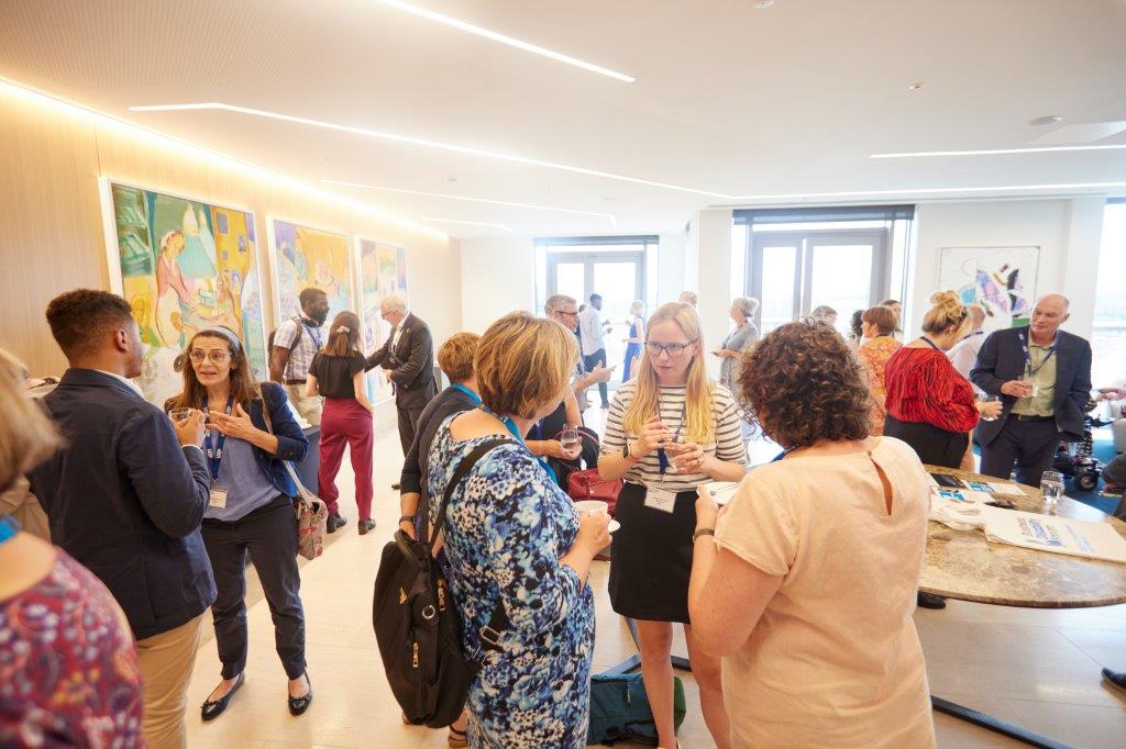 Wide shot of a group of delegates standing and chatting at a daytime event.