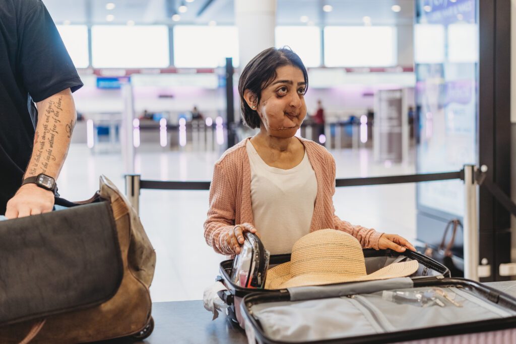 Woman of short stature and with facial difference has her case open ready to be inspected at airport.  